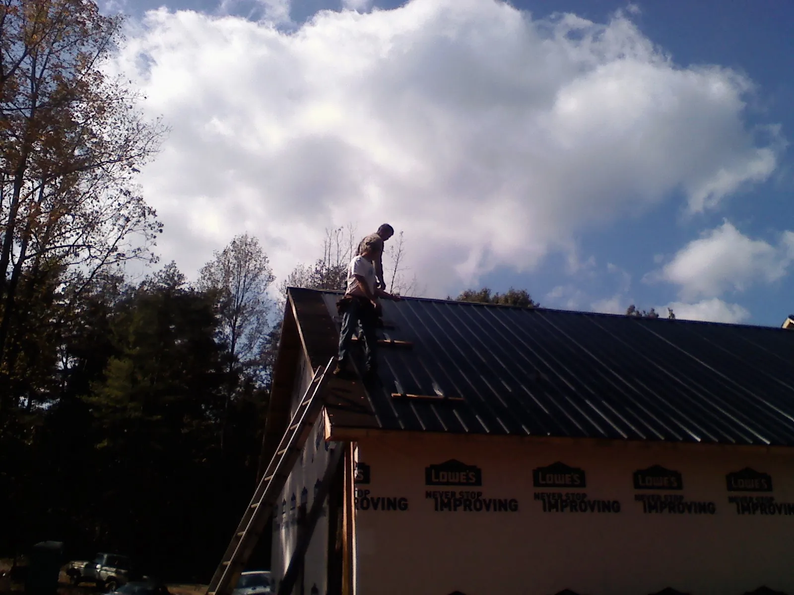 Roofer fastening dark metal panels high against a cloudy sky, from a Roof Inspection job in Montrose